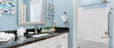 A bathroom with a sink, mirror, and shower. There are towels on the counter and a shower curtain.