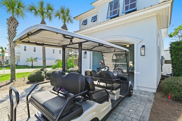 A golf cart with a canopy, parked in front of a building with a white exterior and blue shutters.
