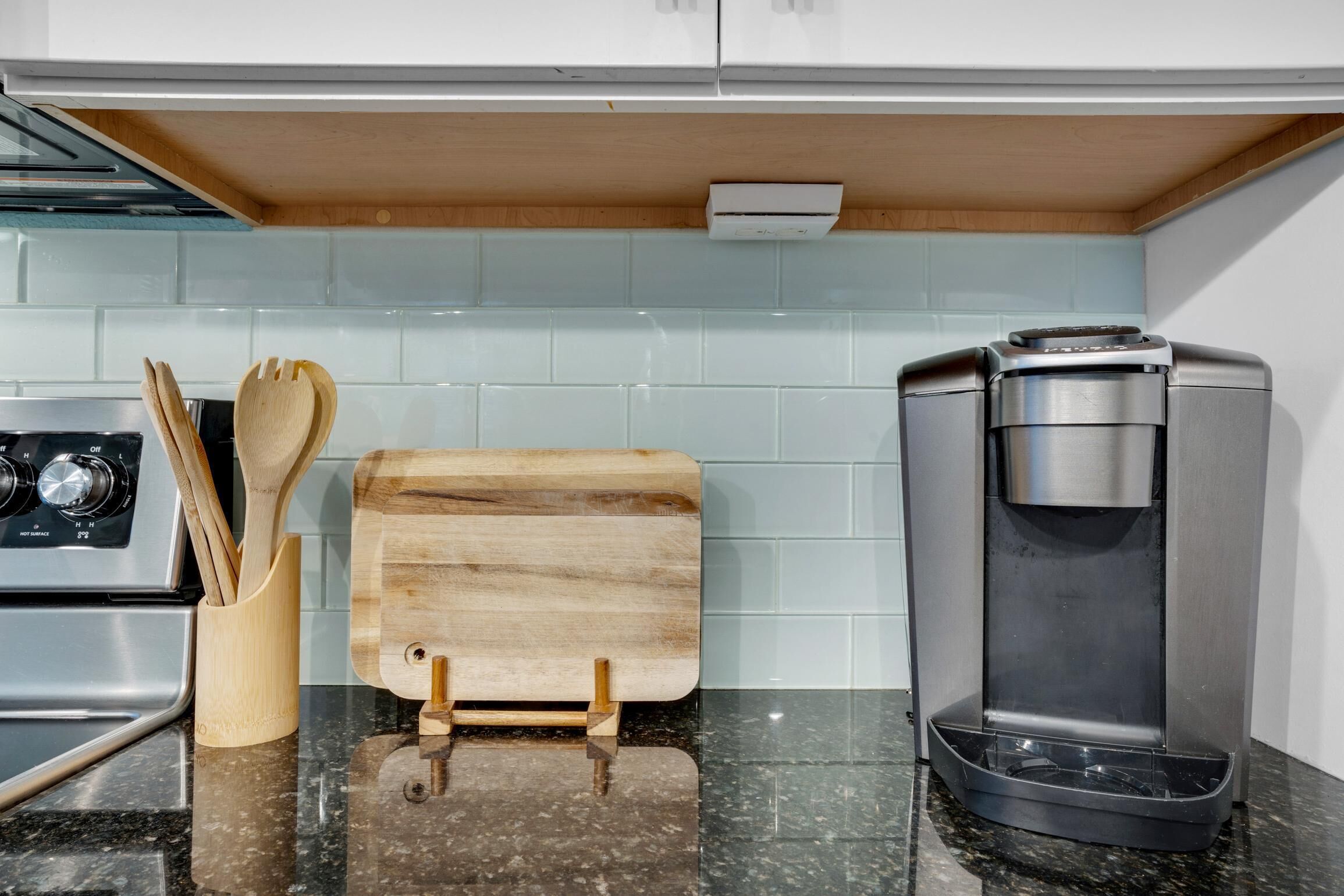 Cucina con piano cottura in acciaio inossidabile, macchina da caffè, utensili in legno e tagliere.