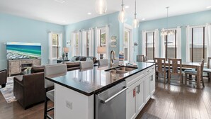 A modern kitchen with a central island, dining area with wooden chairs, and a living room with a sofa and TV. - Fun In The Sun (Miramar Beach)