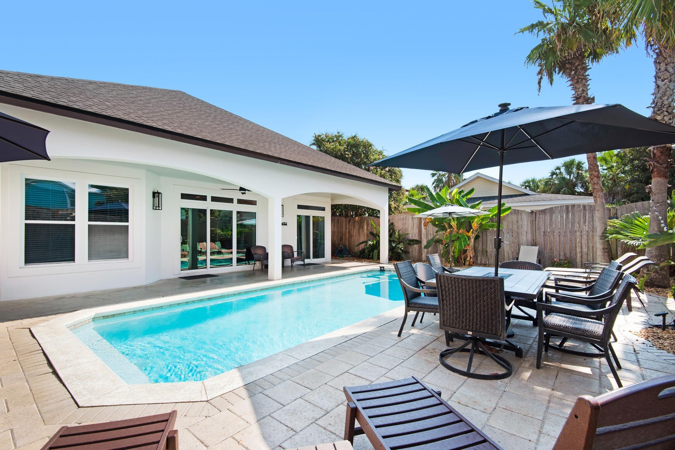 A backyard with a swimming pool, patio furniture, and a covered seating area.