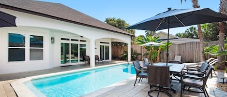 Un patio trasero con piscina, mobiliario de exterior y una zona de estar cubierta.