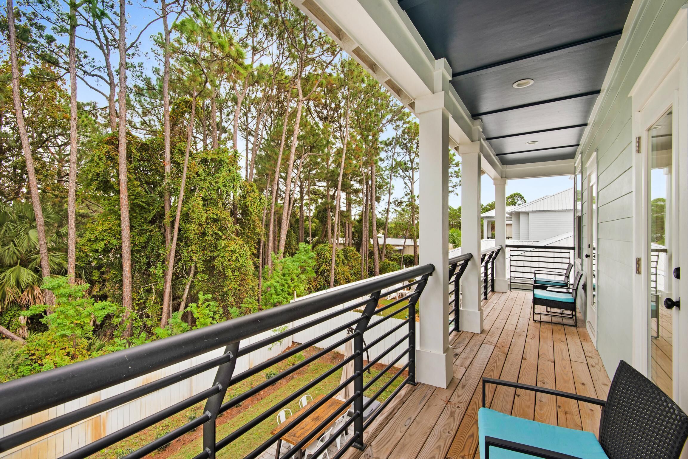 A covered outdoor deck with a wooden floor, black railing, and a view of a forested area.