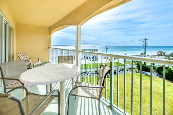 A balcony with a round table and chairs, overlooking a beach and ocean.