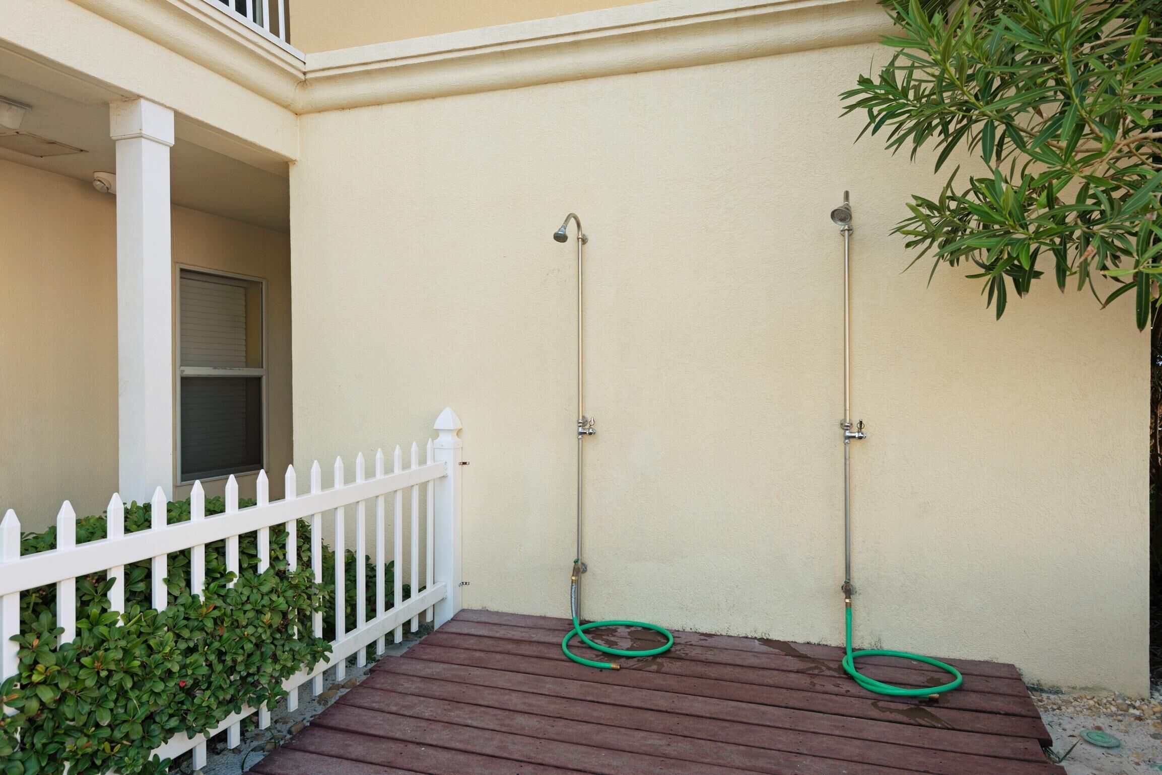 Una terraza de madera con cerca de piquetes blancos, una pared color beige y una manguera verde.