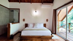 Un dormitorio con una cama de madera, ventilador de techo, equipo de aire acondicionado y un gran ventanal con vistas a follaje.