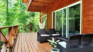 Una terraza de madera con mobiliario de mimbre y una hamaca colgada.