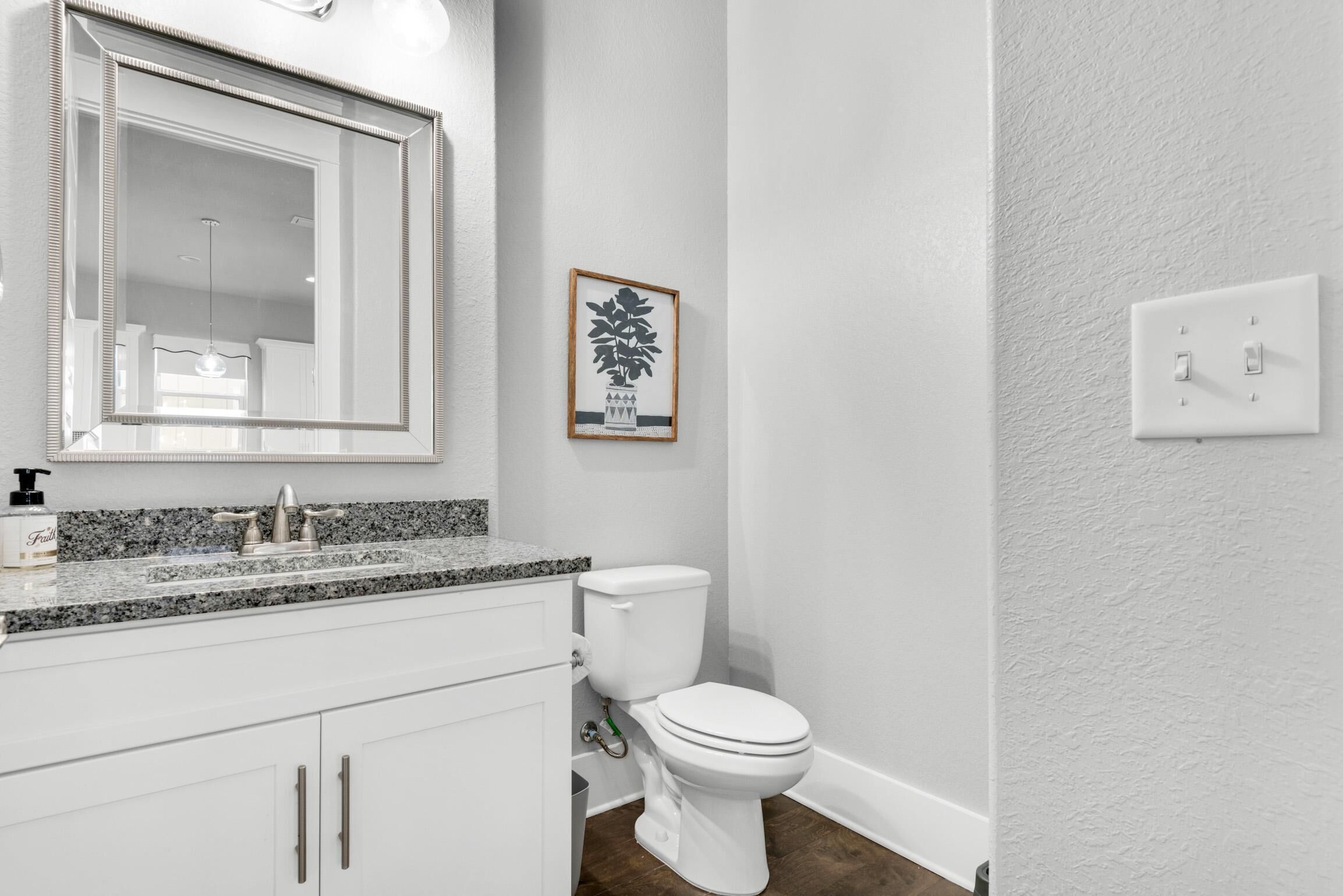 Un baño con lavamanos blanco, un espejo, un inodoro y un cuadro en la pared.