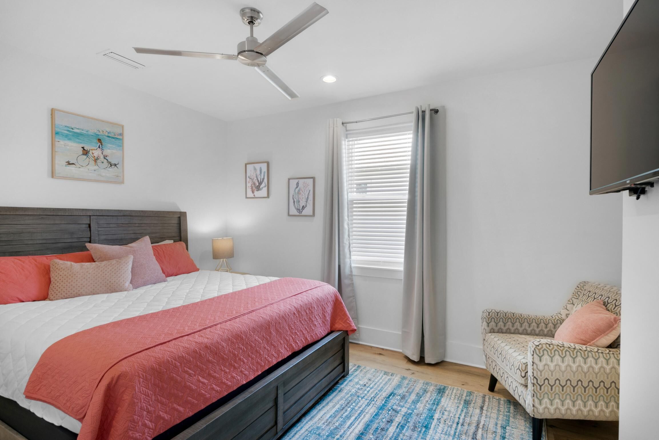 Un dormitorio con cama, ventilador de techo, ventana con cortinas, una silla y decoración en la pared.