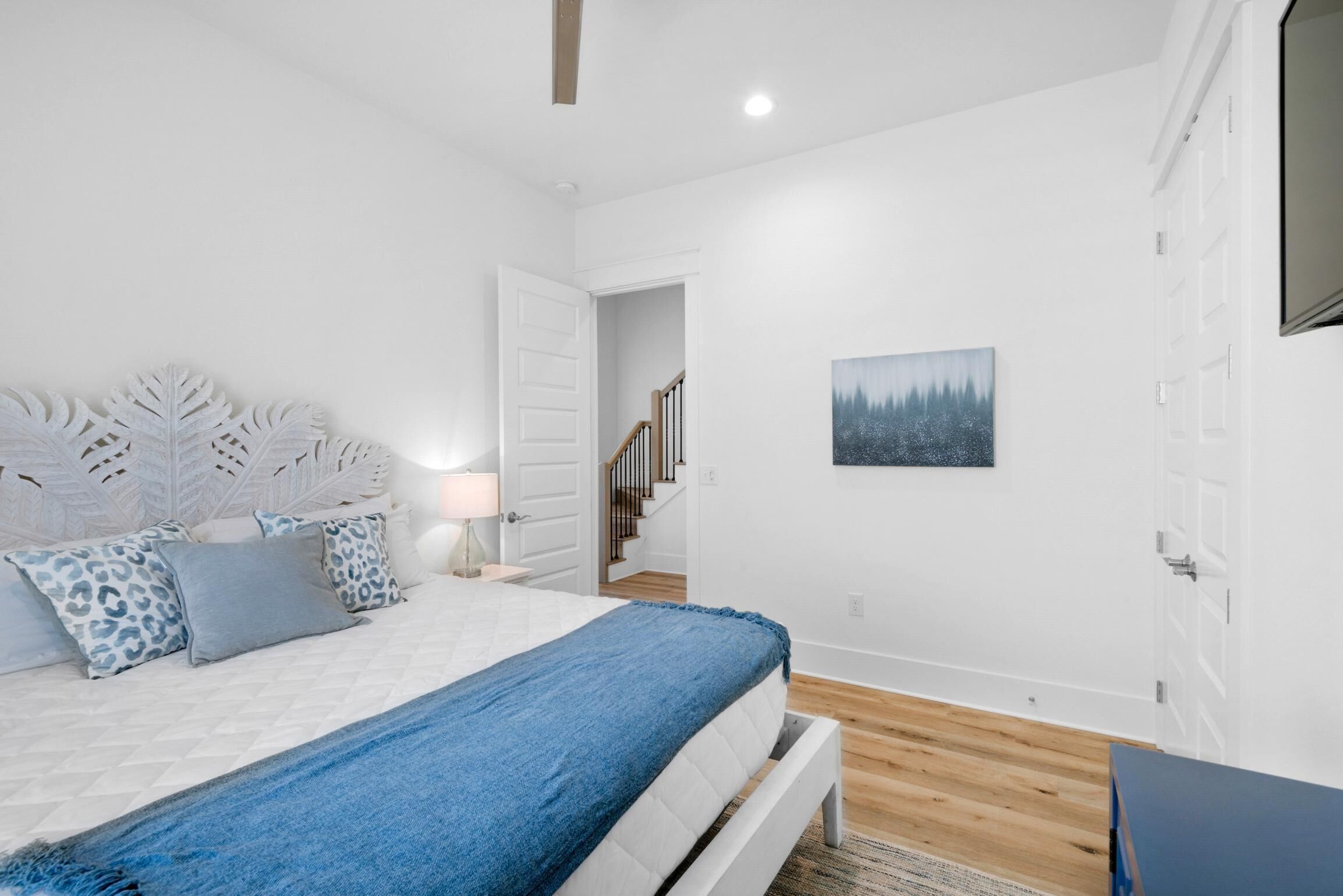 A bedroom with a bed, white walls, a painting, and a staircase.