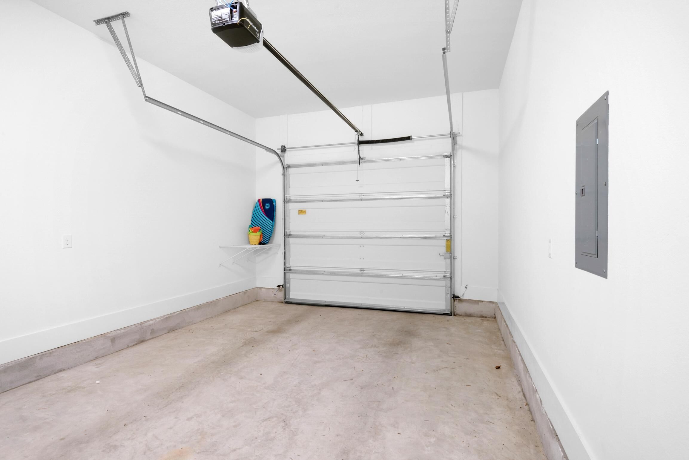 A clean, empty garage with a closed metal door, a ceiling-mounted projector, and a small shelf with a colorful object.