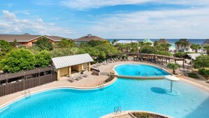 A resort with a large swimming pool, lounge chairs, and a view of the ocean. - Beach Resort 406 (Miramar Beach)