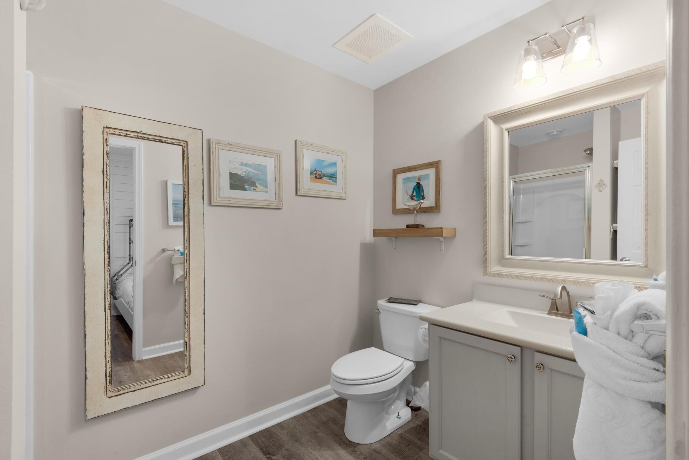 Une salle de bain équipée de toilettes, d’un lavabo et de grands miroirs. Des tableaux encadrés ornent le mur, et un porte-serviettes contient une serviette.