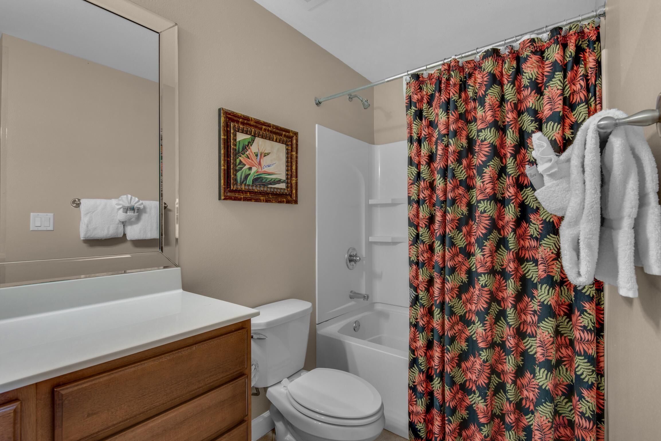 A bathroom with a white toilet, a bathtub, and a shower curtain with a tropical leaf pattern.