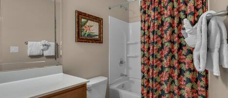 A bathroom with a white toilet, a bathtub, and a shower curtain with a tropical leaf pattern.