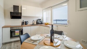 A modern kitchen with white cabinets, a built-in oven, a coffee machine, and a window with a view of the sea. - 1 bedroom awesome apartment in Karlobag (Karlobag)