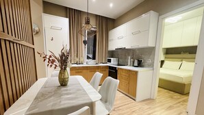 A modern kitchen with white cabinets, a dining area with a marble table, and a sofa in the adjacent living room. - AJ Apartments 3: City Center View Apartment (Tirana)