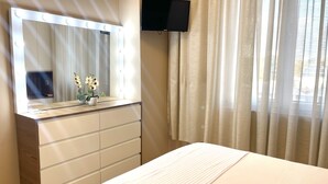A hotel room with a large mirror, a flat-screen TV mounted on the wall, a bed with a striped bedspread, and a window with sheer curtains. - AJ Apartments 3: City Center View Apartment (Tirana)