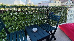 A balcony with a view of buildings, a table with a white object, and green plants. - AJ Apartments 3: City Center View Apartment (Tirana)