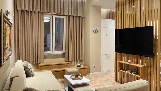 A modern living room with a sofa, a coffee table, a flat-screen TV, and a wooden partition. - AJ Apartments 3: City Center View Apartment (Tirana)