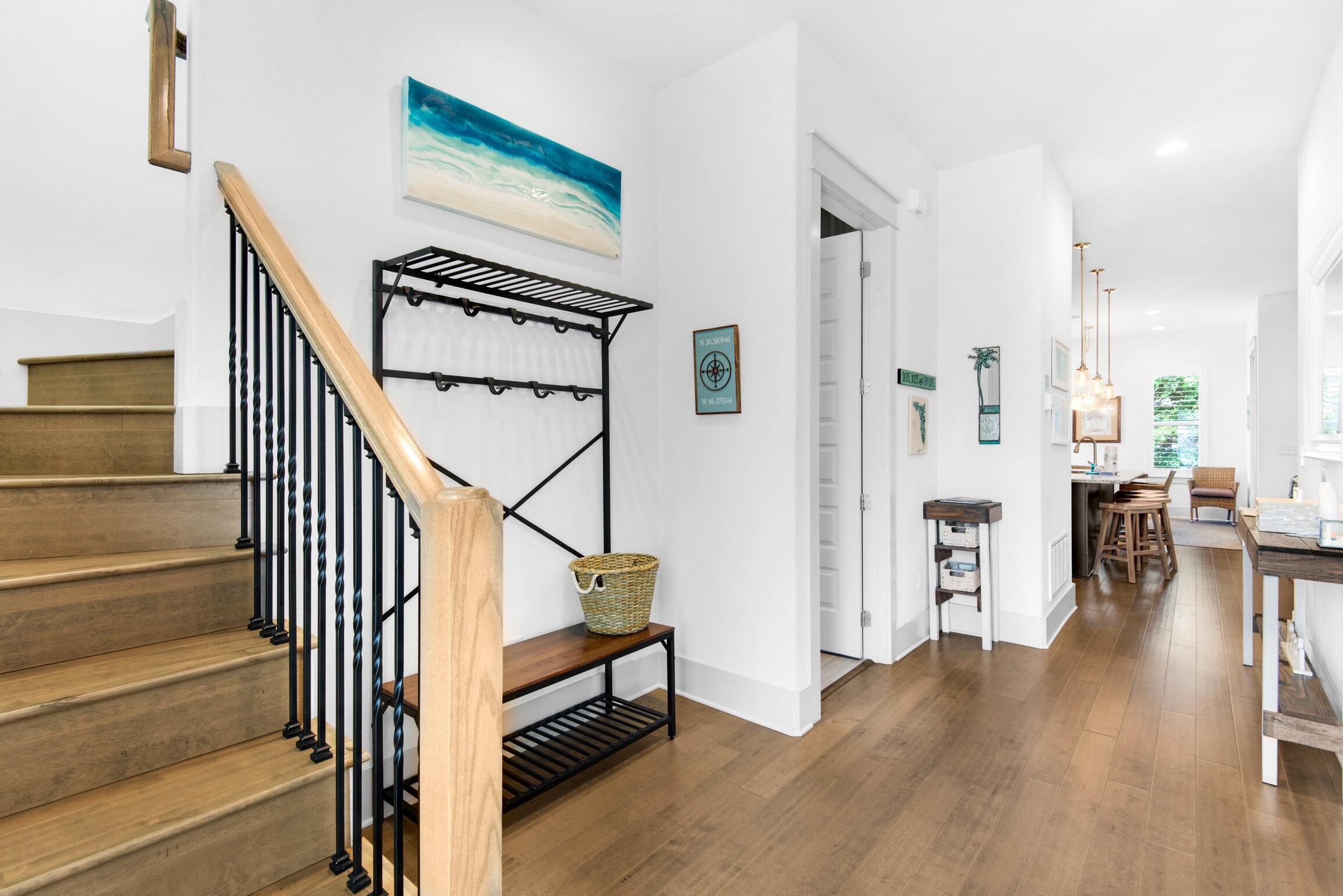 Eine Treppe mit Holzbalkon und Metallspindeln, die zu einem Raum mit weißer Wand und einem Gemälde mit Strandmotiv führt.