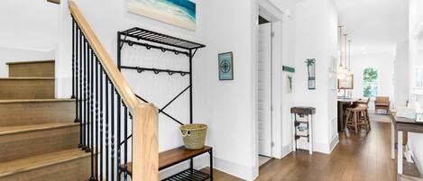 Eine Treppe mit Holzbalkon und Metallspindeln, die zu einem Raum mit weißer Wand und einem Gemälde mit Strandmotiv führt.
