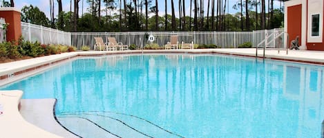A rectangular swimming pool with a white deck and a white fence surrounding it.