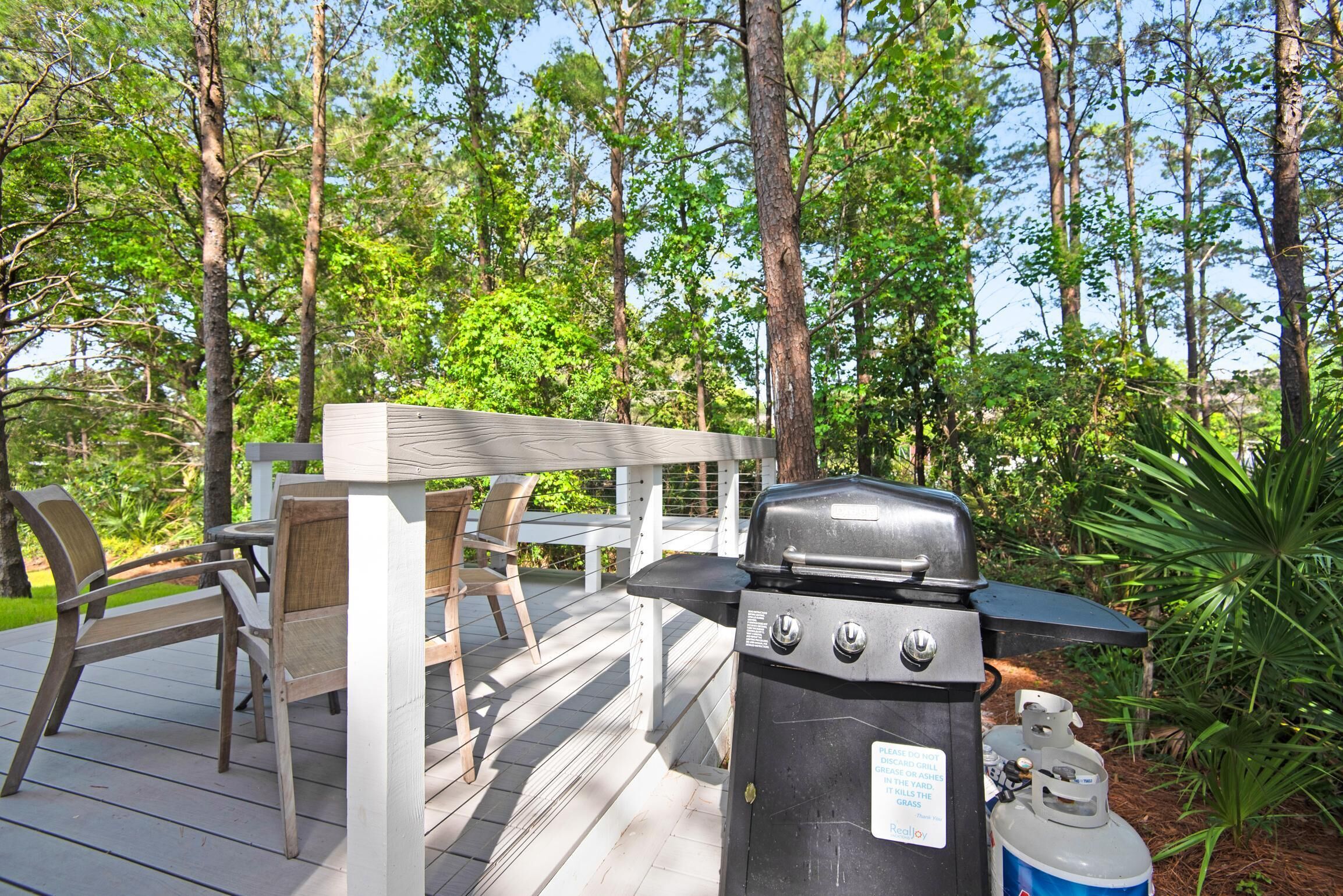 A barbecue grill with a propane tank on a wooden deck surrounded by trees.
