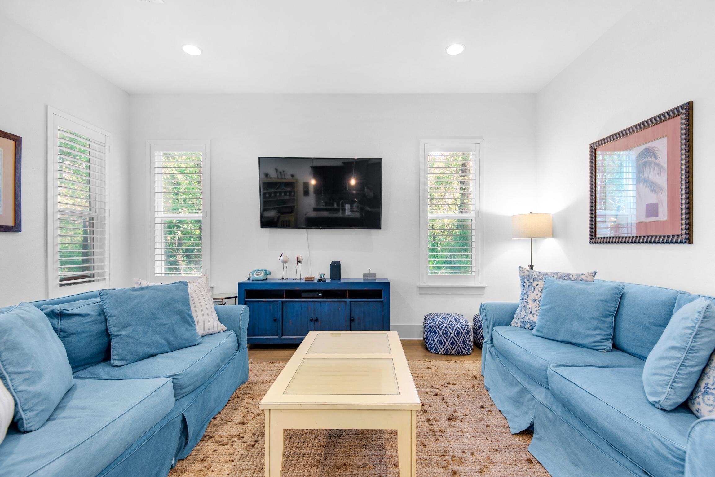 A living room with two blue sofas, a coffee table, a TV on the wall, and a blue cabinet.
