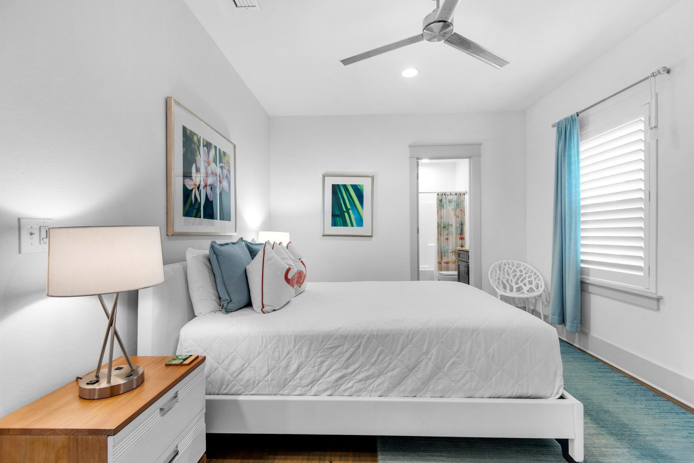 A modern bedroom with a bed, a bedside table with a lamp, a ceiling fan, and a view of a bathroom.