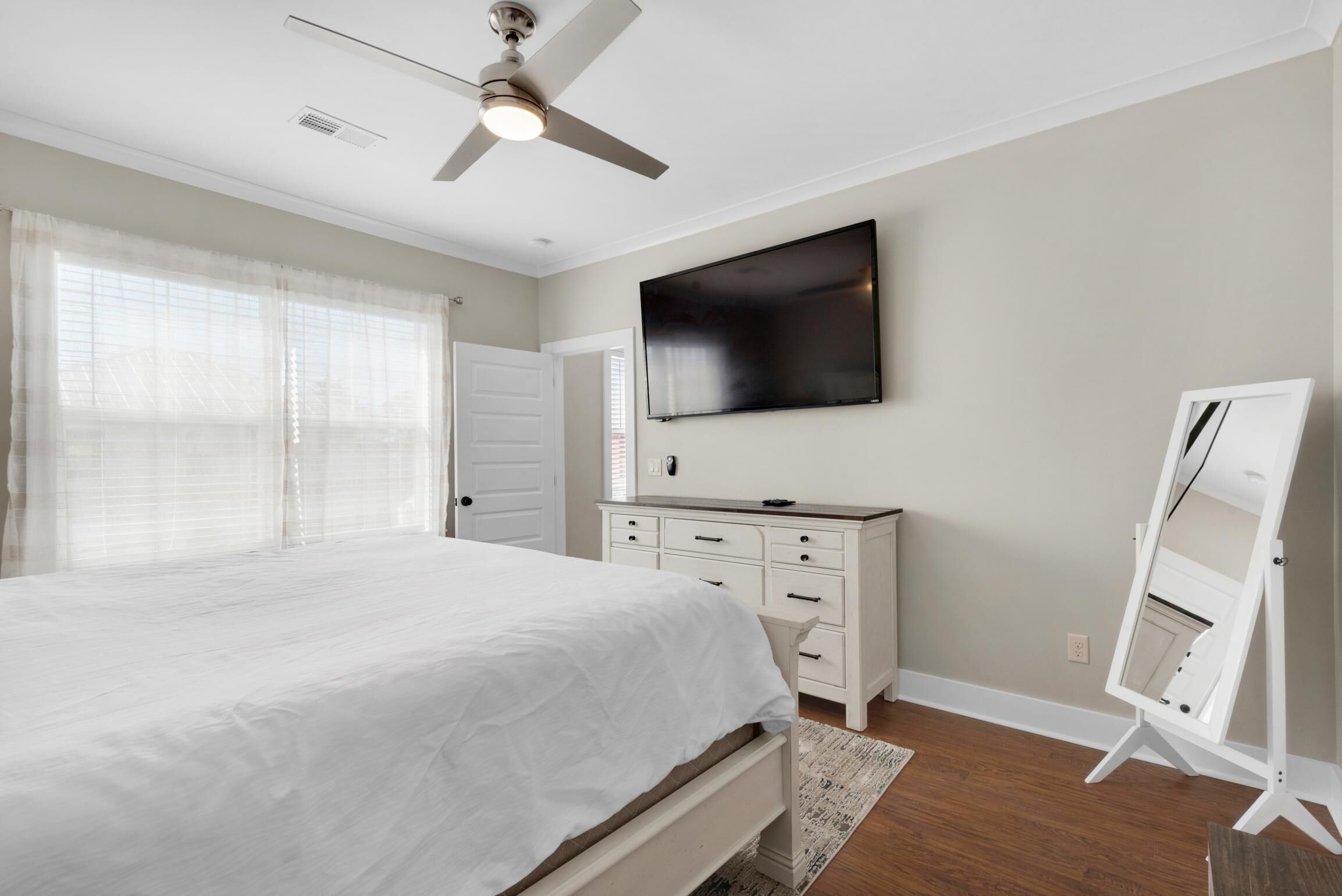 Un dormitorio con cama, cómoda, televisor y ventilador de techo.