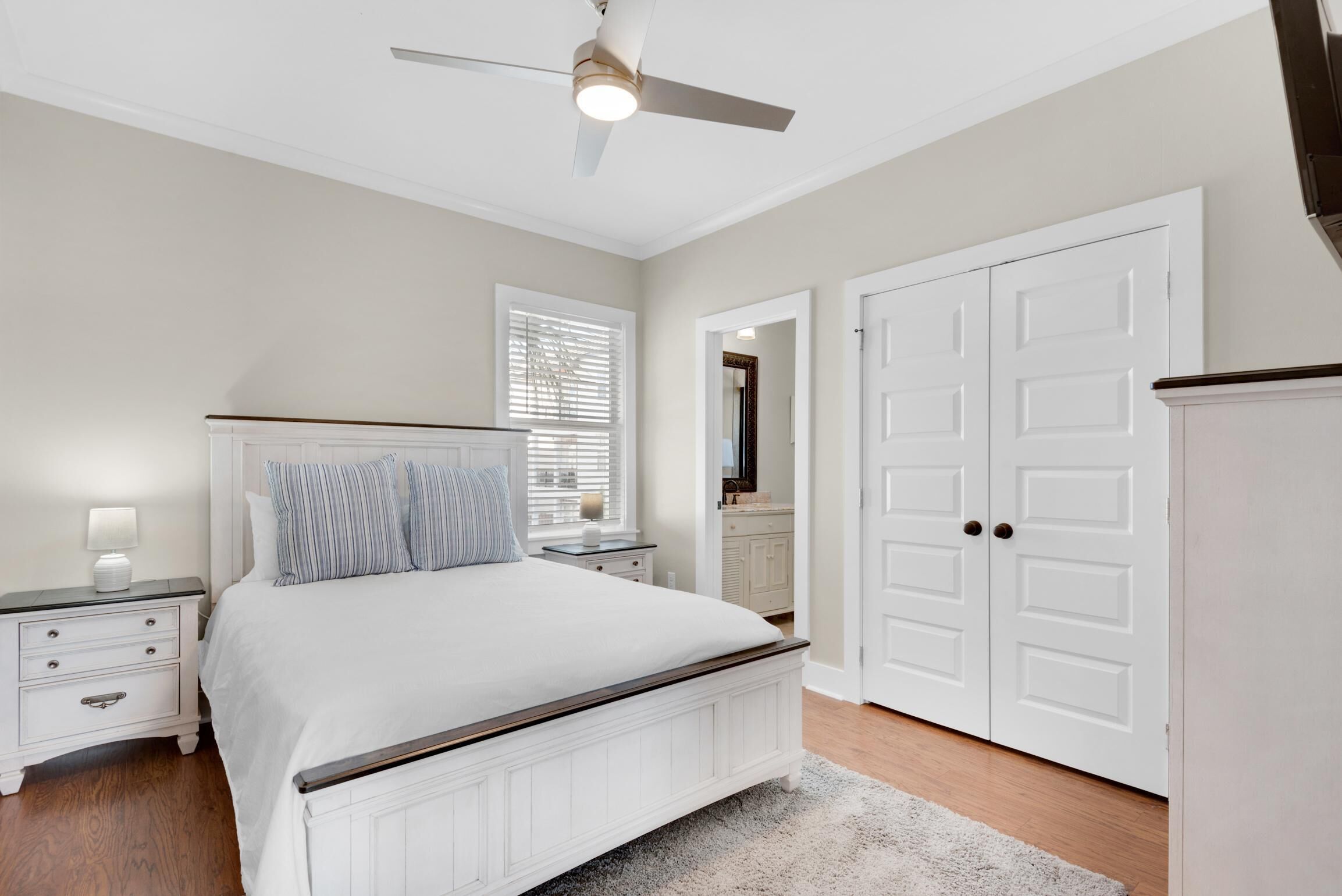A bedroom with a bed, nightstands, a ceiling fan, a wardrobe, and a window with blinds.