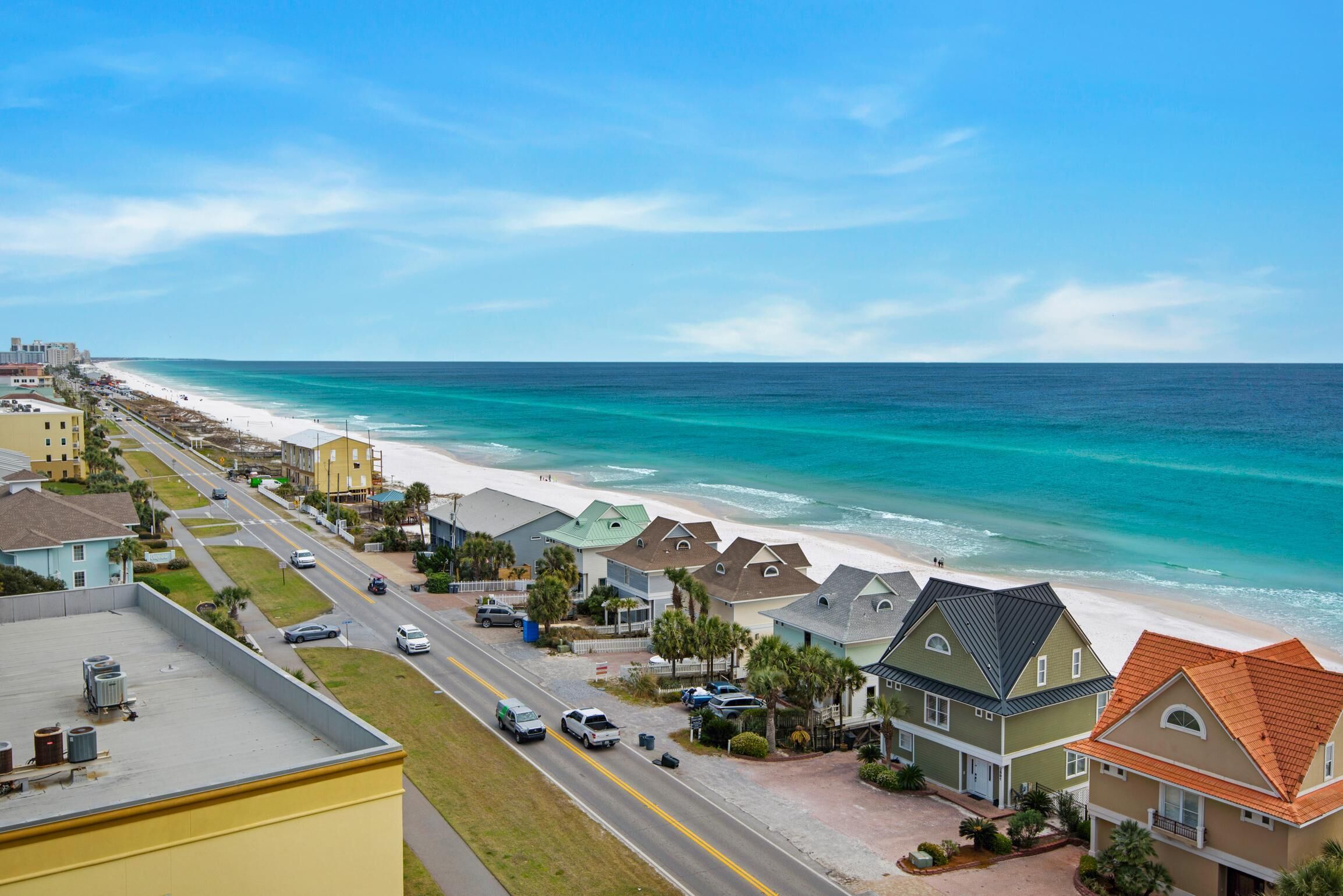 A coastal residential area with houses along the beach, a clear road, and a view of the ocean.