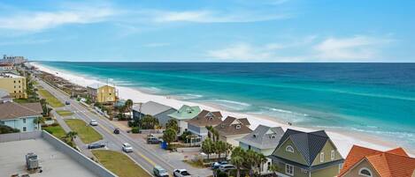 A coastal residential area with houses along the beach, a clear road, and a view of the ocean.