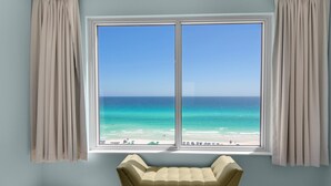 A room with a large window overlooking a beach, a beige sofa, and light blue walls. - Leeward Key 903 (Miramar Beach)