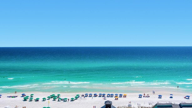 A beach with white sand and a clear blue sky. There are several umbrellas and people on the beach. - Leeward Key 903 (Miramar Beach)