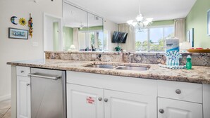 A modern kitchen with a granite countertop, stainless steel appliances, and a large window offering a view of the outdoors. - Leeward Key 204 (Miramar Beach)
