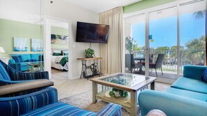 A spacious living room with a large TV, comfortable seating, a glass coffee table, and a view of the outdoors. - Leeward Key 204 (Miramar Beach)