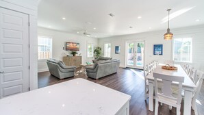 A spacious living room with a large white marble island, grey sofas, and a dining area with white chairs and a table. - Fins Up (Destin)