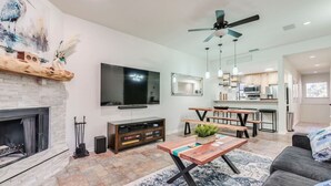 A modern living room with a fireplace, a flat-screen TV, a wooden coffee table, and a dining area with benches. - Comal Condo - Riverfont Complex Across from Schlitterbahn (New Braunfels)