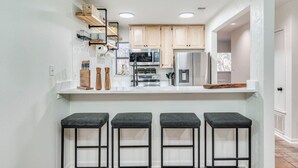 A modern kitchen with wooden cabinets, a stainless steel refrigerator, and a bar stool seating area. - Comal Condo - Riverfont Complex Across from Schlitterbahn (New Braunfels)