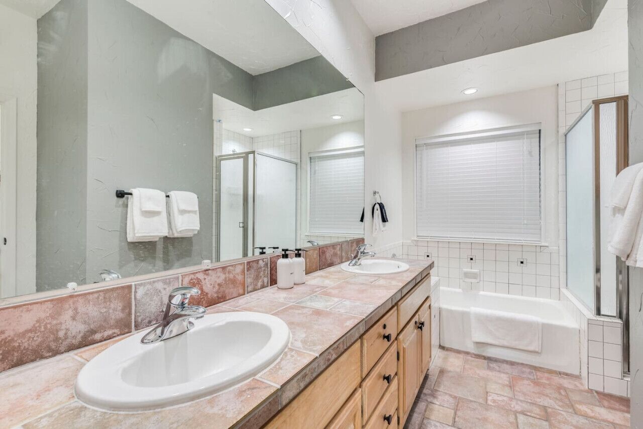 Un baño moderno con dos lavamanos, un espejo grande, una bañera y una ducha.