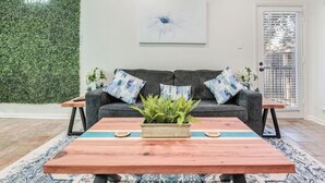 A living room with a grey sofa, a wooden coffee table, and a green wall with a plant. - Comal Condo - Riverfont Complex Across from Schlitterbahn (New Braunfels)