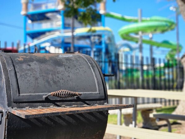 A black grill with a spring mechanism, set against a background featuring a water slide and a fence. - Comal Condo - Riverfont Complex Across from Schlitterbahn (New Braunfels)