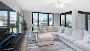 A modern living room with a sectional sofa, a flat-screen TV, and a ceiling fan.