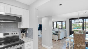 A modern kitchen with a built-in oven and microwave, a dining area with a table and chairs, and a living room with a sofa and a TV.