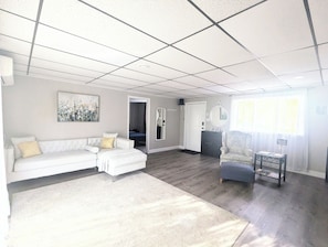 Uma sala de estar com um sofá branco, uma poltrona azul, uma mesa de centro e um quadro na parede.