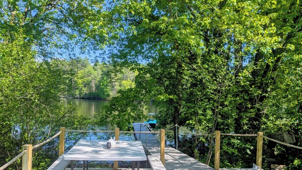 A wooden deck with picnic tables overlooking a calm lake, surrounded by dense greenery. - Maine river escape: free kayaks, paddle boards, tennis, cute rabbits and fun! (West Gardiner)