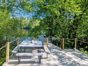 A wooden deck with picnic tables overlooking a calm lake, surrounded by dense greenery. - Maine river escape: free kayaks, paddle boards, tennis, cute rabbits and fun! (West Gardiner)