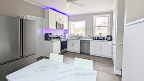 A modern kitchen with a refrigerator, stove, microwave, and toaster. There is a dining table with chairs and a ceiling fan. - Maine river escape: free kayaks, paddle boards, tennis, cute rabbits and fun! (West Gardiner)